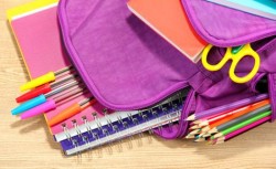 Purple backpack with school supplies on wooden background